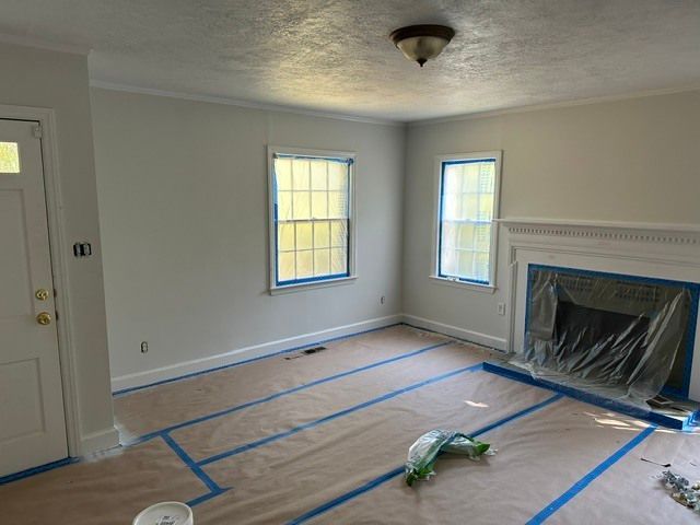 Empty living room with taped floor covering, two windows, and a fireplace under renovation