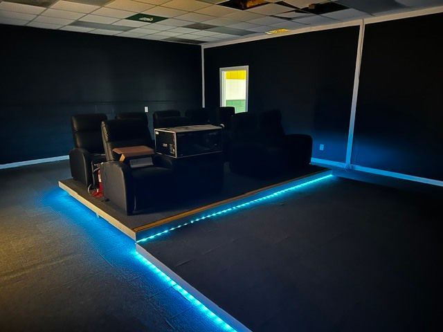 Dark room with a raised seating area outlined by blue LED strip lights and a bright doorway.