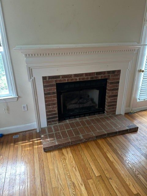 Brick fireplace with white mantel and dark hearth in a room with hardwood floors.