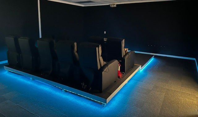 Dark home theater with black reclining seats and blue LED floor lighting