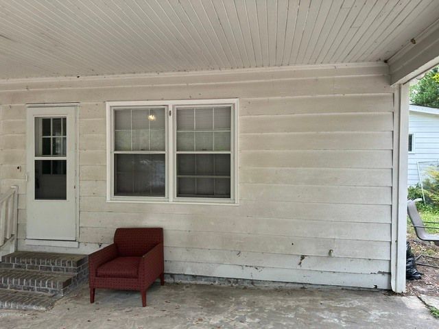 Front porch with white siding, a red chair, and a window beside a screened door