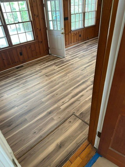 Wood-paneled room with new gray wood-look flooring and large windows and doors.