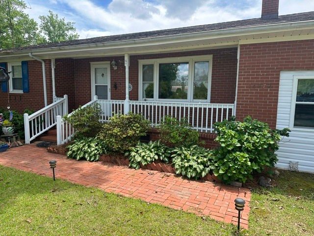 Brick house front porch with white railing, brick walkway, and lush green shrubs