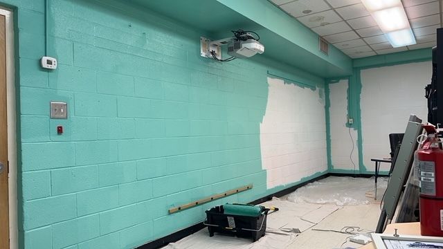 Empty teal room under renovation with tools, debris, and a ladder against the wall