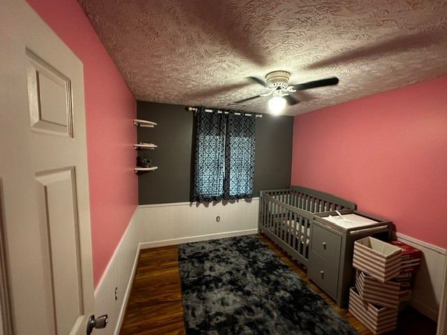 Empty pink nursery with crib, dark rug, window, and ceiling fan.