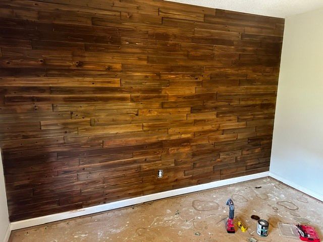 Wood-paneled accent wall in an unfinished room with paint supplies on the floor