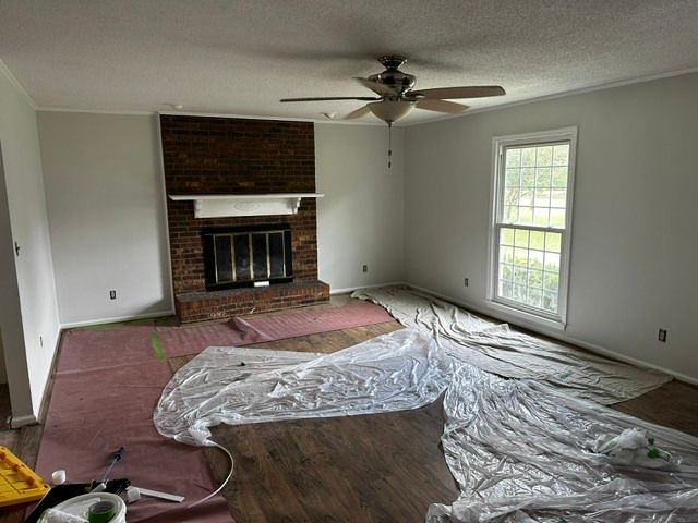 Empty living room with brick fireplace, ceiling fan, and plastic-covered floor during renovation