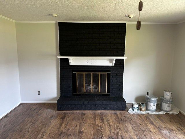 Empty living room with black brick fireplace, wood floor, and paint cans near the wall