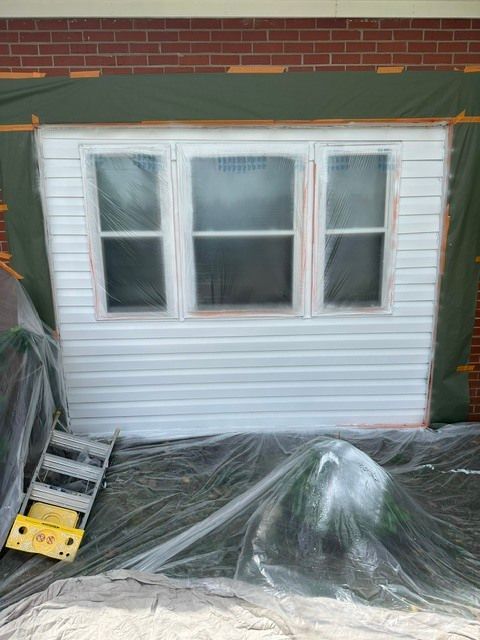 White-sided house wall with three windows, covered in plastic sheeting during exterior work.