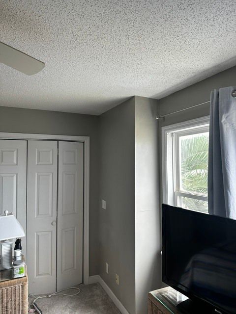 Small bedroom corner with closet doors, TV by a window, and gray walls.