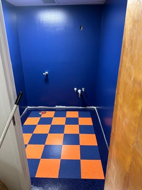 Small blue room with a blue-and-orange checkered floor and exposed wall pipes.