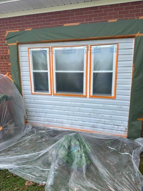 Exterior of a house with three windows boarded by plastic sheeting and wrapped in green trim, under renovation