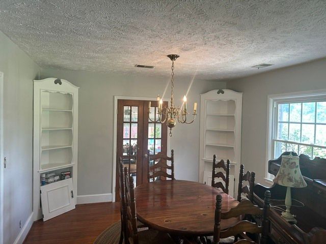 Dining room with oval wood table, chairs, chandelier, and built-in shelves on either side of French doors.