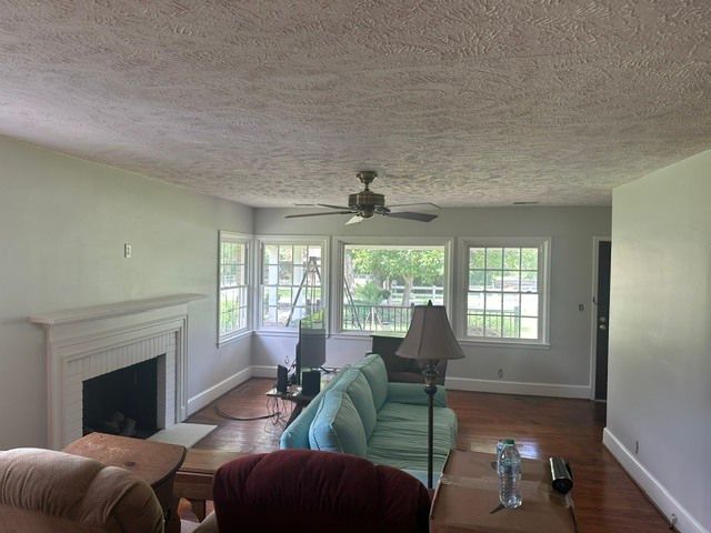 Bright living room with white fireplace, green sofa, ceiling fan, and large windows overlooking a deck.