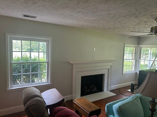 Living room with white fireplace, two windows, and upholstered chairs in soft natural light