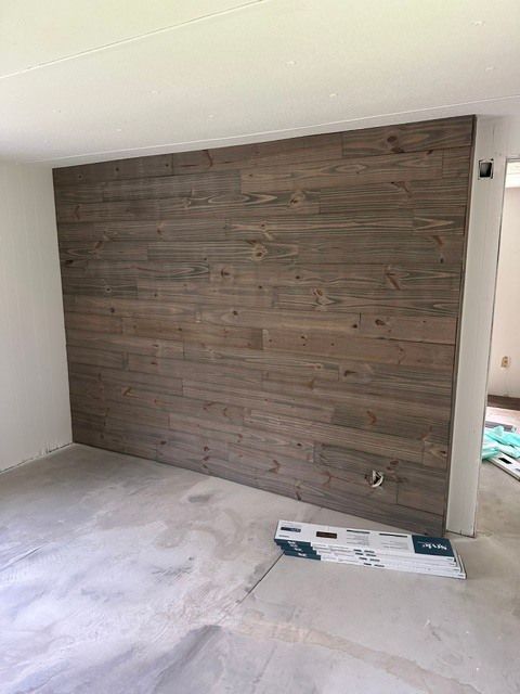Empty room with a large wood-paneled accent wall and unfinished floor and ceiling.
