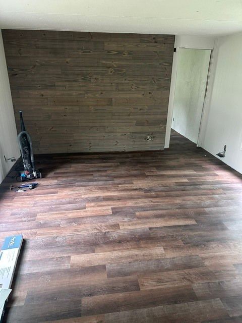 Empty room with dark wood floors and a wood-paneled accent wall at the far end.