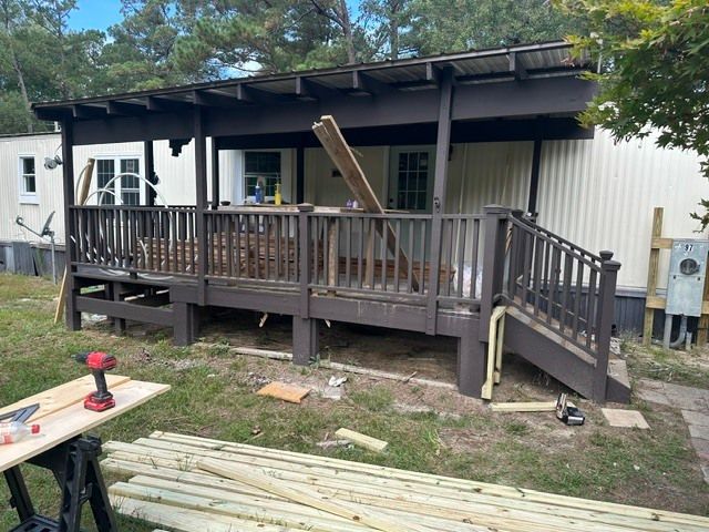 Damaged wooden porch with broken railing, ramp, and debris outside a house under trees.