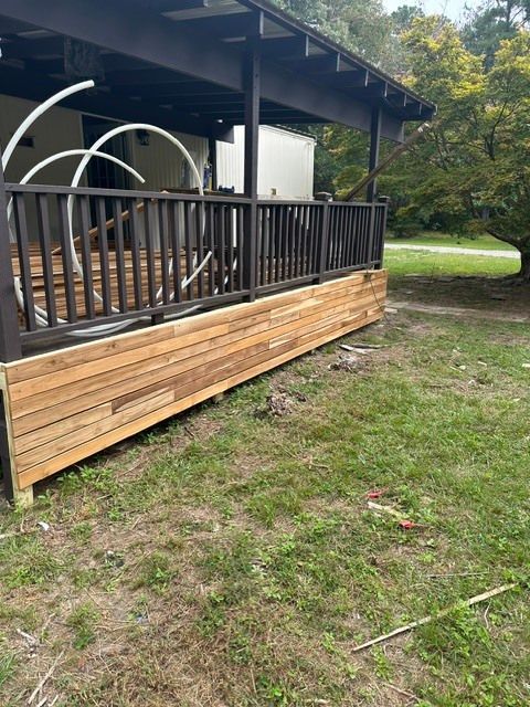 Wooden porch deck with black railing and outdoor chairs beside a grassy yard and trees