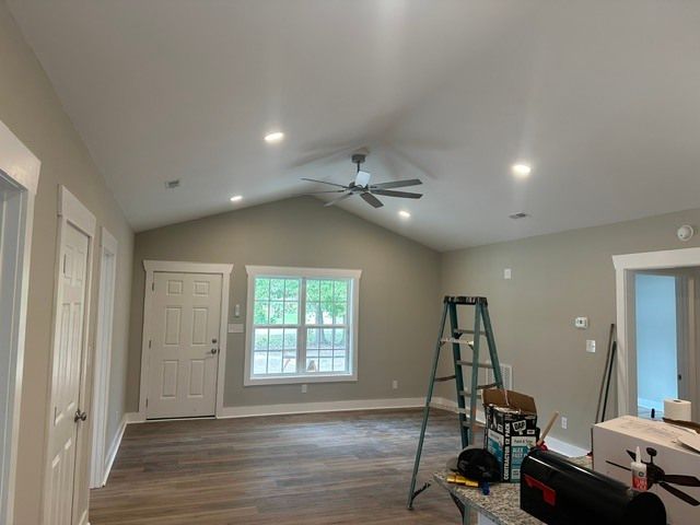 Empty living room with vaulted ceiling, ceiling fan, windows, and a ladder during renovation.