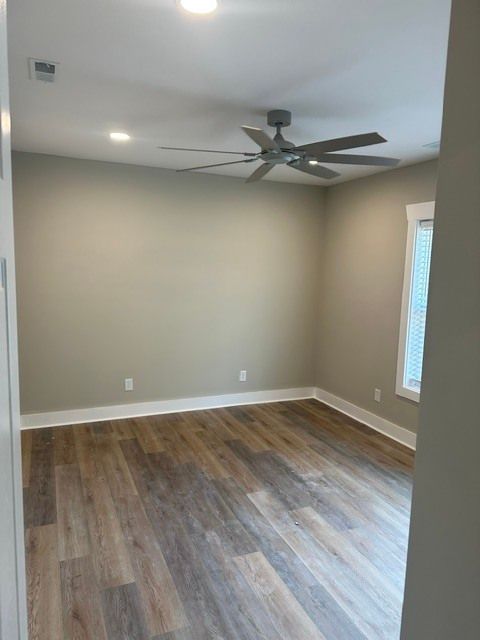 Empty bedroom with wood-look floors, gray walls, ceiling fan, and a small window.