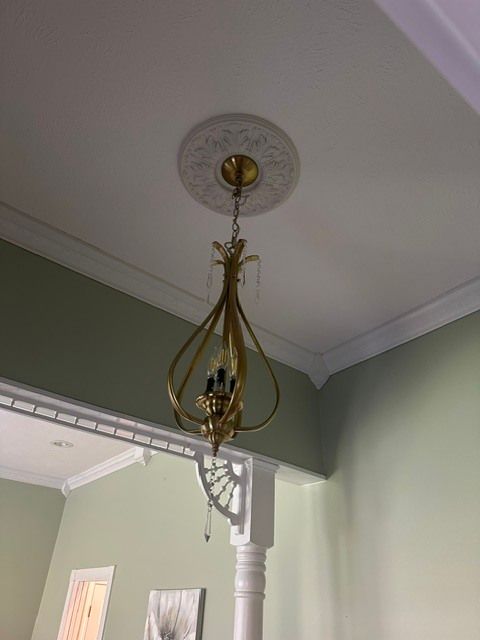 Brass hanging ceiling light with curled cords in a room with pale green walls and white trim