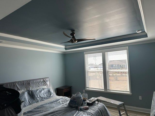 Empty bedroom with gray walls, tray ceiling, ceiling fan, window blinds, bed, and bench.