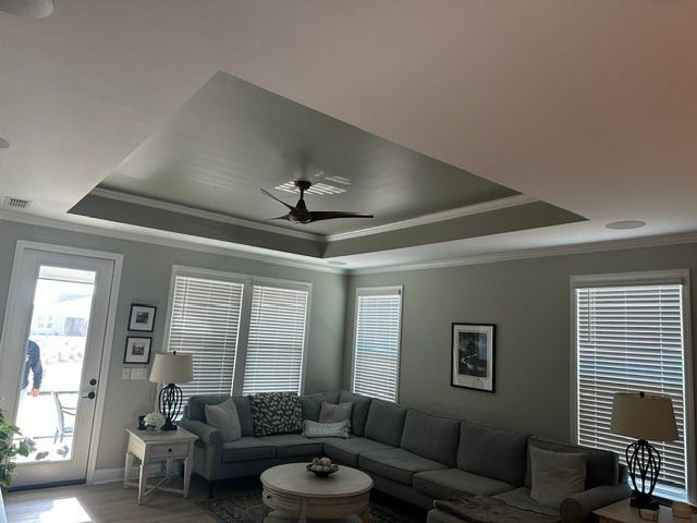 Bright living room with gray sectional, ceiling fan, windows, and a white front door
