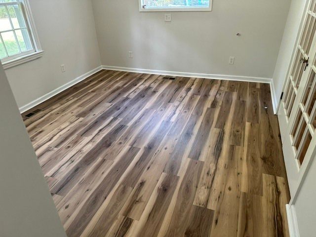Empty room with wood-look flooring, white walls, two windows, and French doors