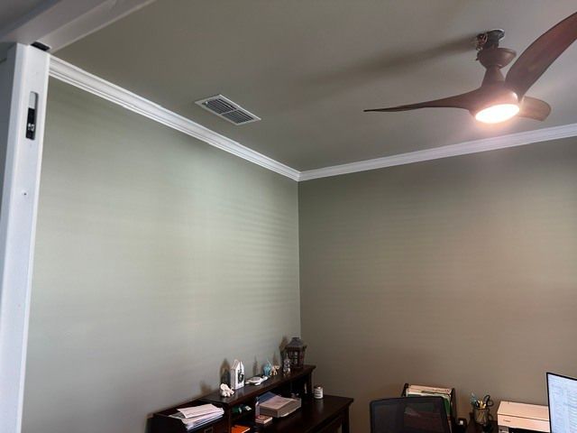 A small room with pale green walls, a ceiling fan, and a desk with a computer in the corner.