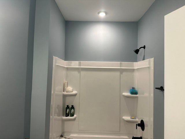 White shower stall with built-in shelves, teal soap, and gray bathroom walls under a ceiling light