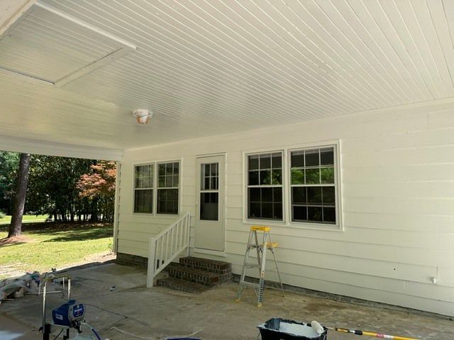 Covered porch with white siding, three windows, small steps, and a ladder near the wall.