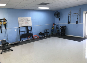 Empty gym room with blue walls, exercise equipment, whiteboard, and a wall fan