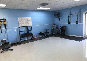 Empty gym room with blue walls, exercise equipment, and black mats along the back wall