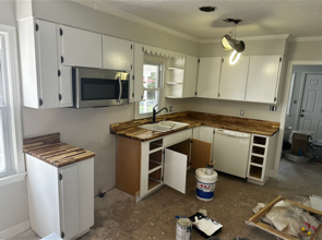 Partially renovated kitchen with white cabinets, wood countertops, and exposed flooring materials