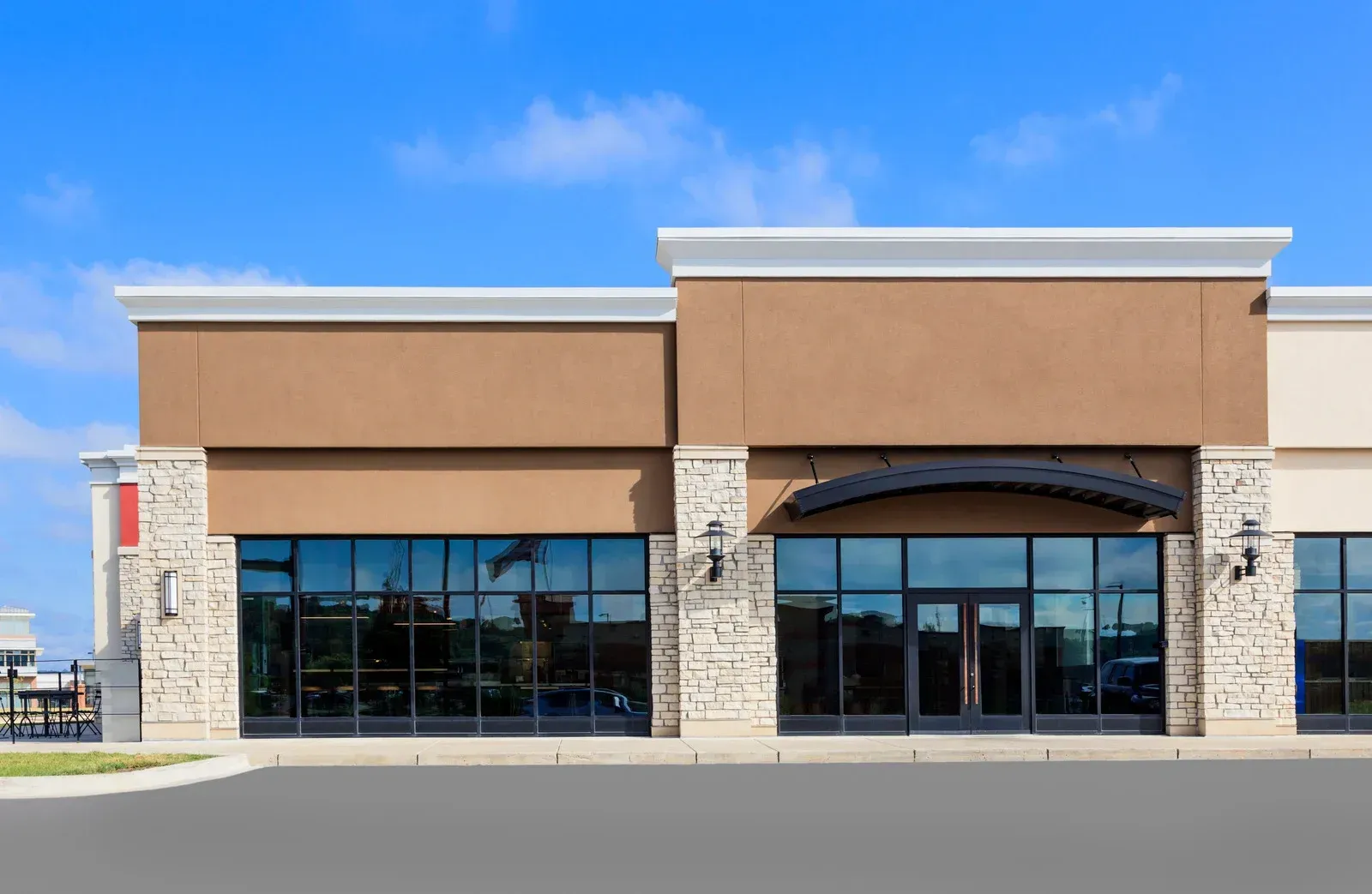 Empty storefront with tan facade, stone columns, and large dark windows under a blue sky
