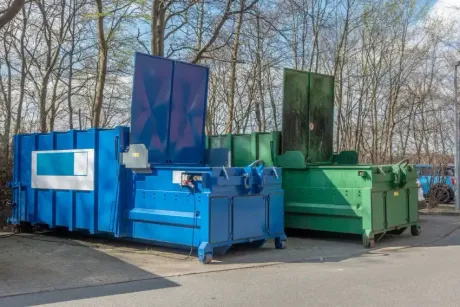 Blue and green industrial recycling balers lined up outdoors near trees
