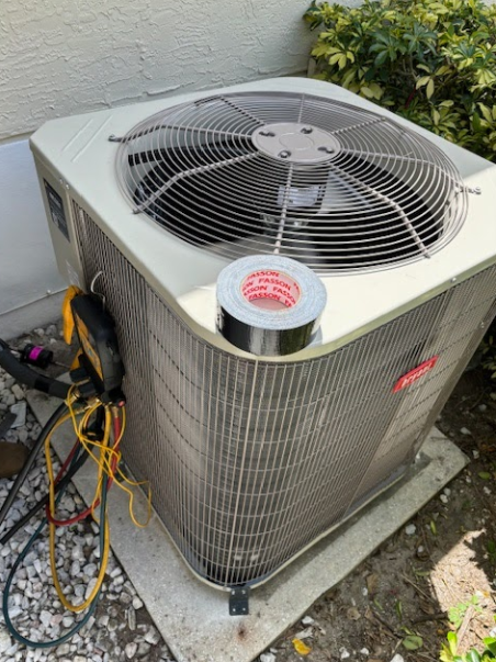 An air conditioner is sitting on the ground next to a roll of tape.