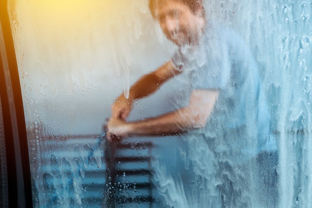 Man pressure washing a window inside house view