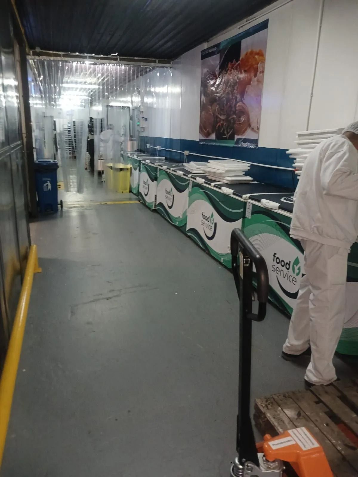 Pasillo industrial con largas encimeras blancas y verdes, un trabajador con equipo de protección
