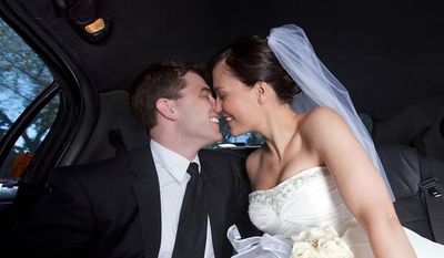 Novios besándose en el asiento trasero de un coche, la novia con vestido blanco y velo.