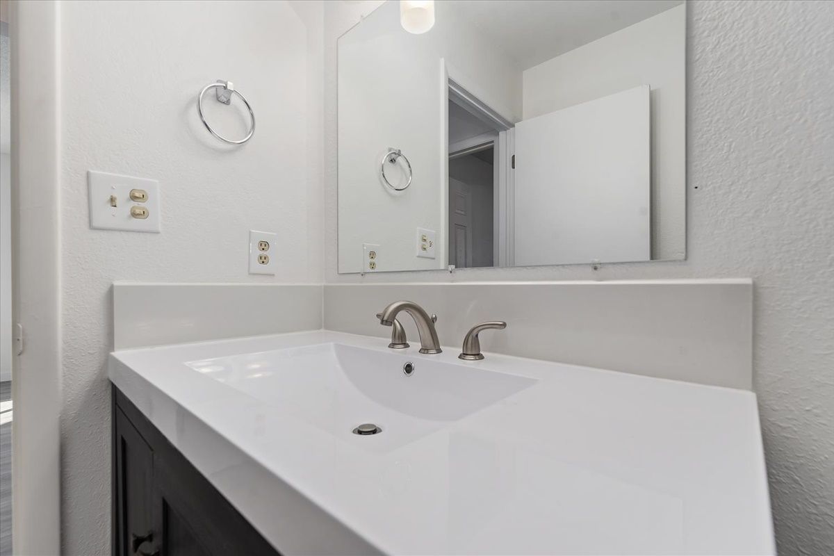 White bathroom sink and countertop with faucet, mirror, and towel ring.