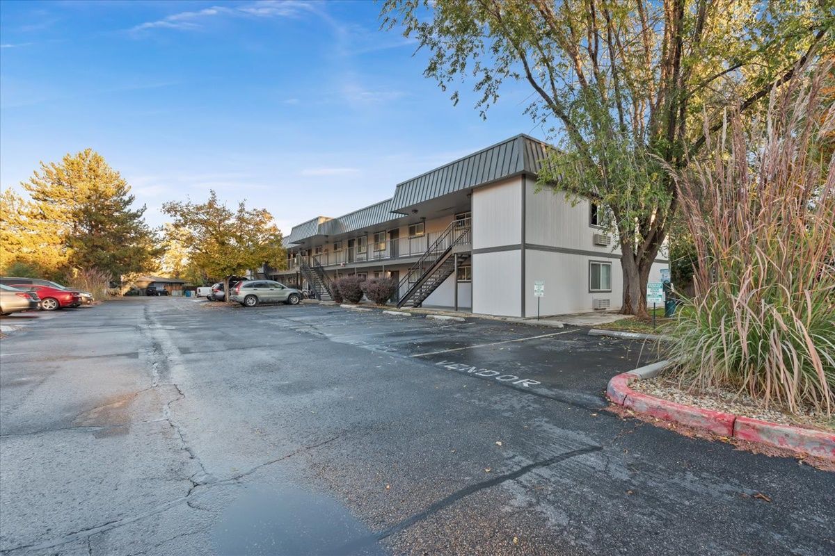 Apartment building with outdoor staircases, asphalt parking lot, trees, and cars.