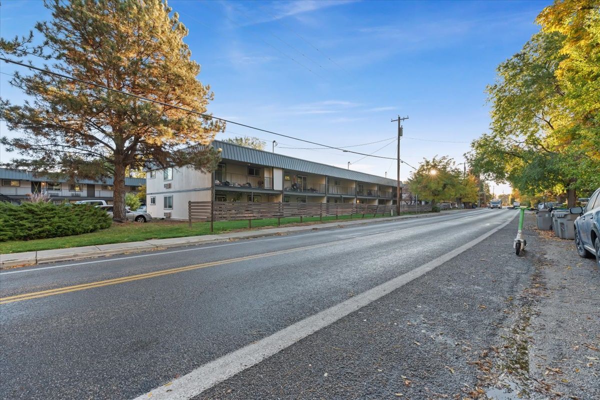 Street view of a two-story building with a line of parked cars on the side of the road and trees.