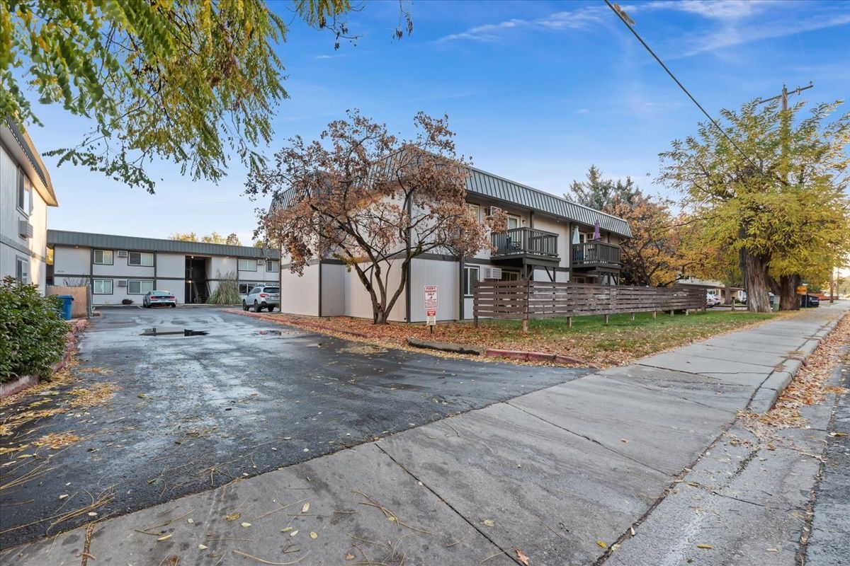 Apartment building exterior, asphalt parking area and sidewalk, overcast sky.