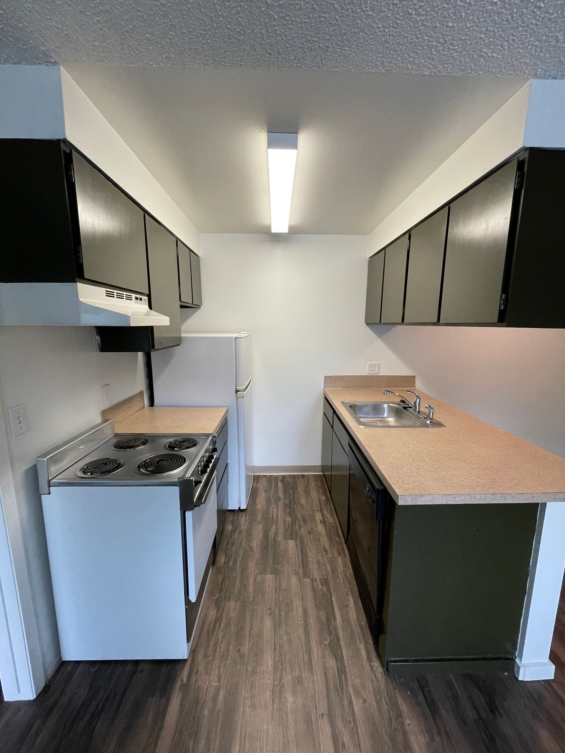 A small kitchen with dark upper cabinets, white appliances, and a wood-look floor.