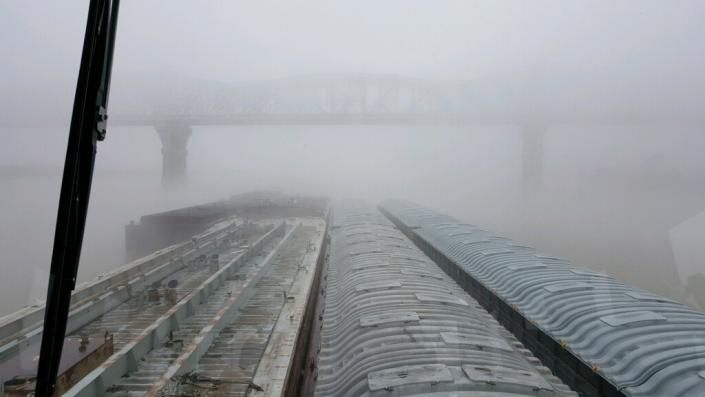 Freight train cars shrouded in heavy fog under a bridge.