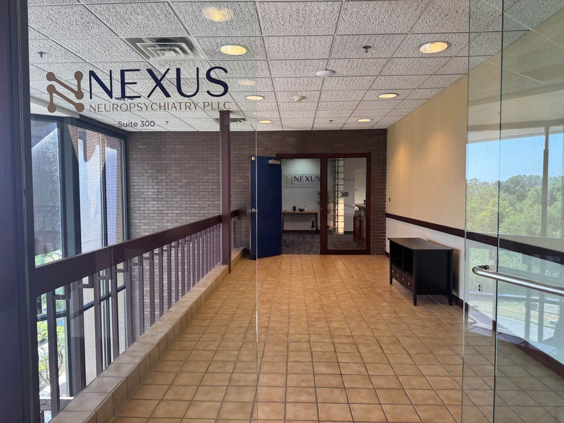 A long hallway with brick walls, beige tile floor, and glass doors. The Nexus logo is in the top left corner.