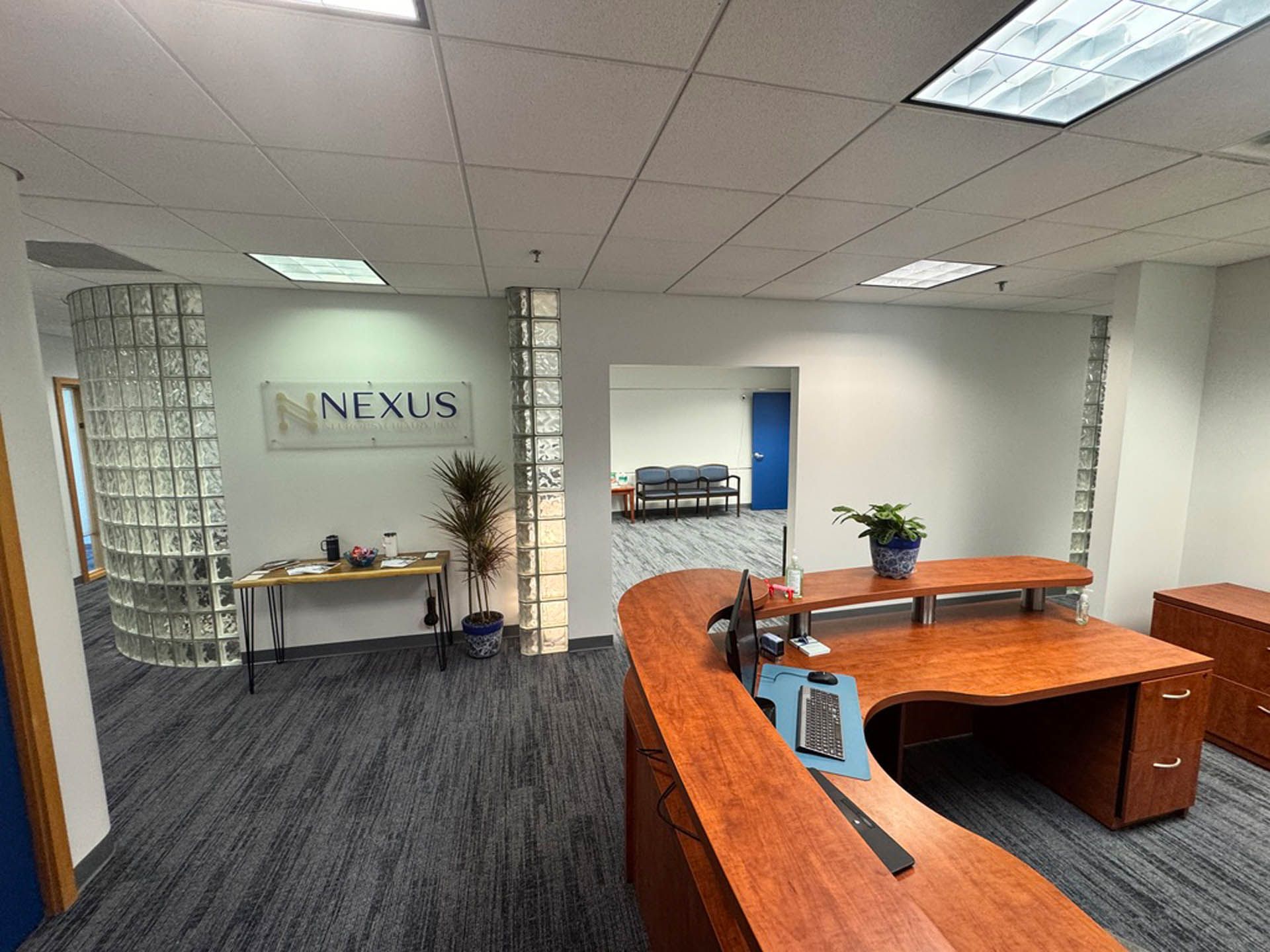 Office reception area with curved wooden desk, Nexus sign, and glass block wall.