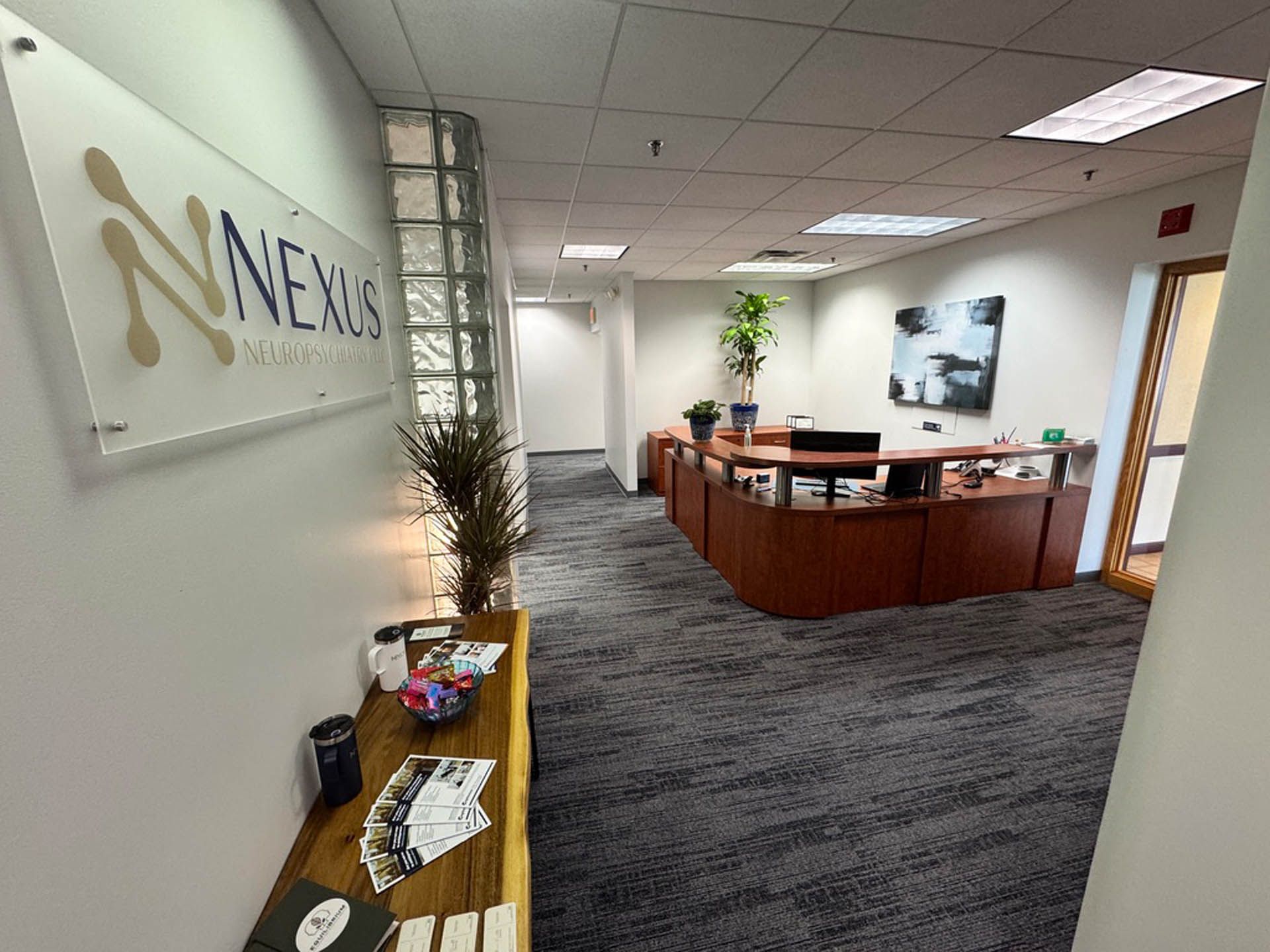 Office reception area with the Nexus logo on the wall, desk, and a hallway with gray carpet.